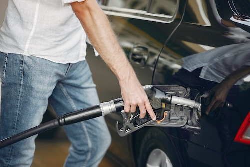 man in white shirt and jeans fills car with gasoline pump