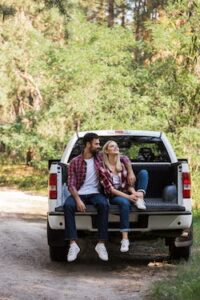 couple hugging and sitting together on pickup truck in forest